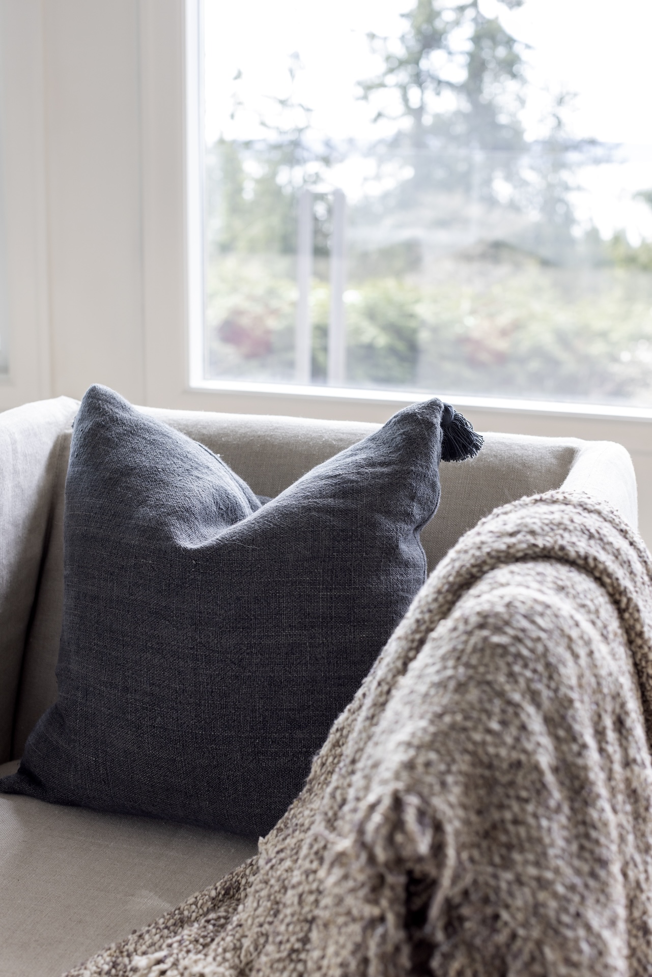 megan baker interiors luxury interior design west coast reno detail of a chunky knit throw with brown and white colour charcoal grey linen pillow and forest view through the window in the background