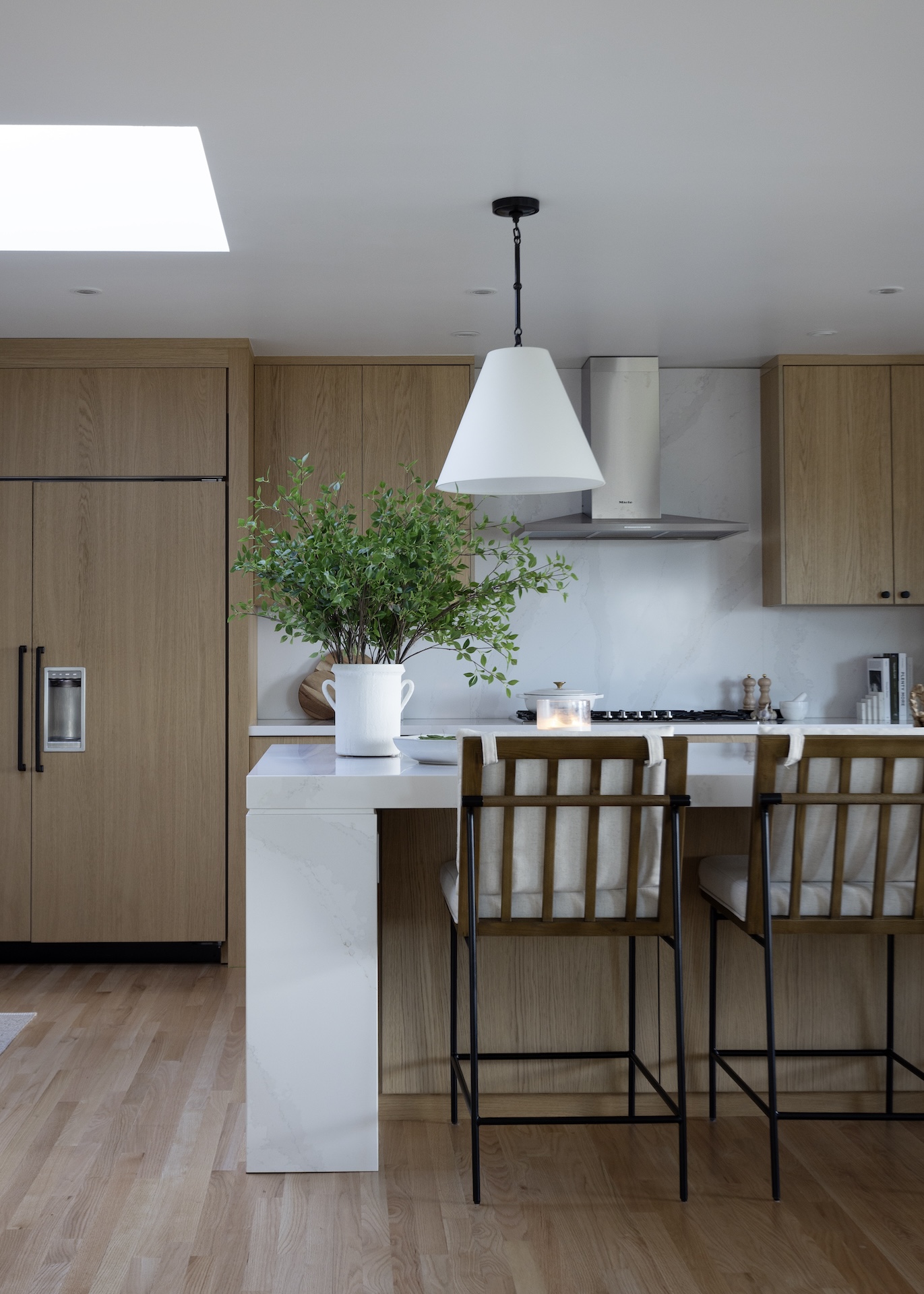 megan baker interiors luxury interior design west coast reno modern kitchen design with warm white oak cabinets white linen pendants over kitchen island white marble kitchen island with modern thick waterfall sides and lived in bar stools with shaker back and black metal legs origninal thin plank oak floors