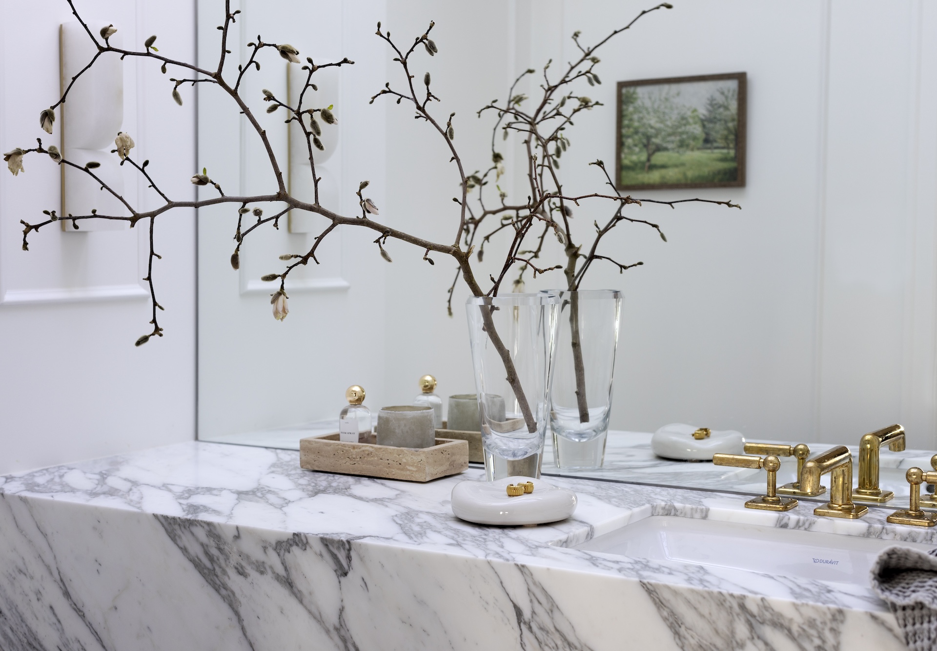 megan baker interiors luxury interior design west coast reno megan baker interiors custom powder room design with french wall moulding white walls a wall to wall mirror grey vein marble strong pattern countertop magnolia branch in a crystal vase and travertine tray with candle and perfume on display organic ceramic dish hold gold jewelry and aged natural brass faucet from waterworks