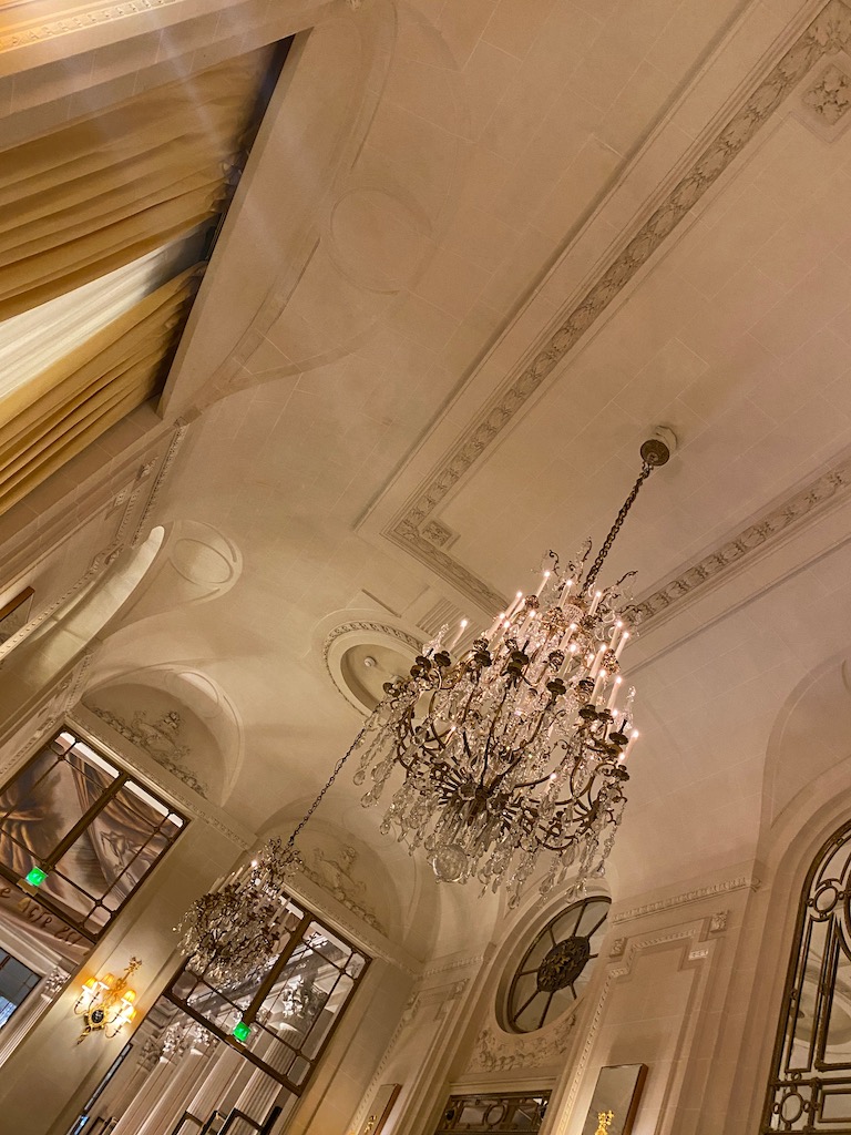 ceiling moulding at a historic hotel in paris. Le Meurice Hotel Paris. White ceiling with french moulding and rococo details. Large antique chandelier, tall windows with antique glass, gold drapery, glowing lights